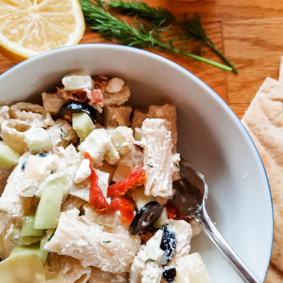 Tatziki Pasta Salad in a white bowl with a fork on a wood counter.