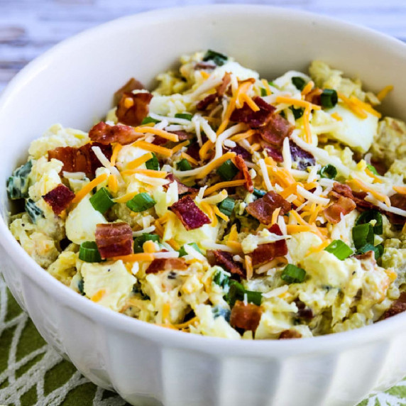 Loaded Cauliflower Potato Salad shown in serving bowl on green-white background.