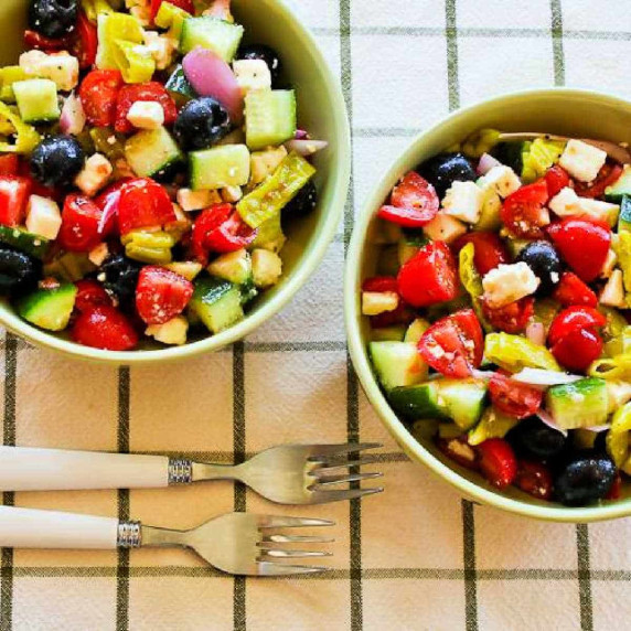 Chopped Greek Salad with Peperoncini shown in two serving bowls with forks.