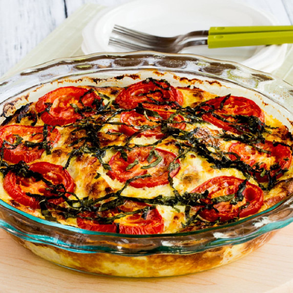 Crustless Three-Cheese Tomato-Basil Quiche shown in baking dish with plates and forks in back.