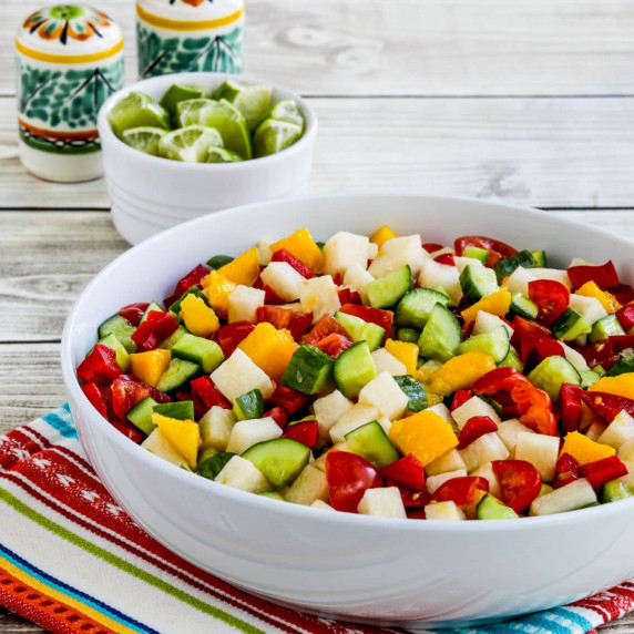 Jicama salad with jicama, cucumber, tomato, mango, and bell pepper, shown in serving bowl with lime 
