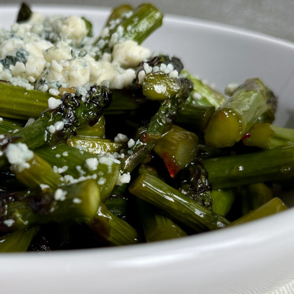 Sauteed asparagus in a white bowl topped with blue cheese crumbles.