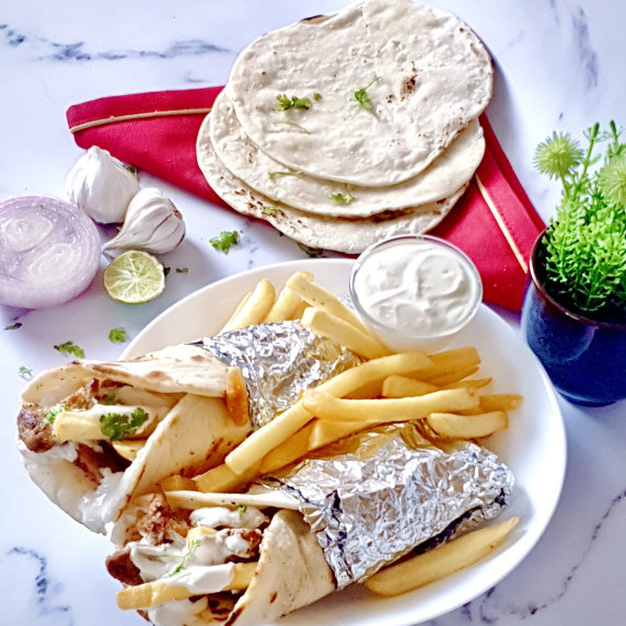 Two easy chicken shawarma wraps with creamy garlic sauce and French fries on a white plate.