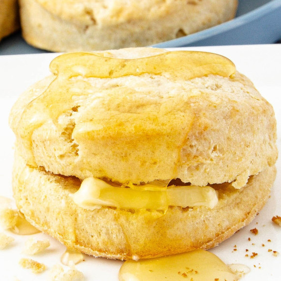 A golden biscuit sliced open with a pat of butter inside, being drizzled with honey.