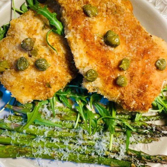 chicken coated in breadcrumbs with capers and asparagus on the bed of rocket