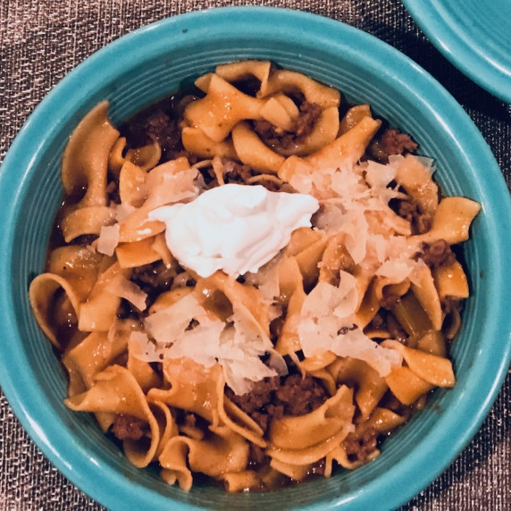 Beef Stroganoff in a blue bowl with a dollop of sour cream on top.