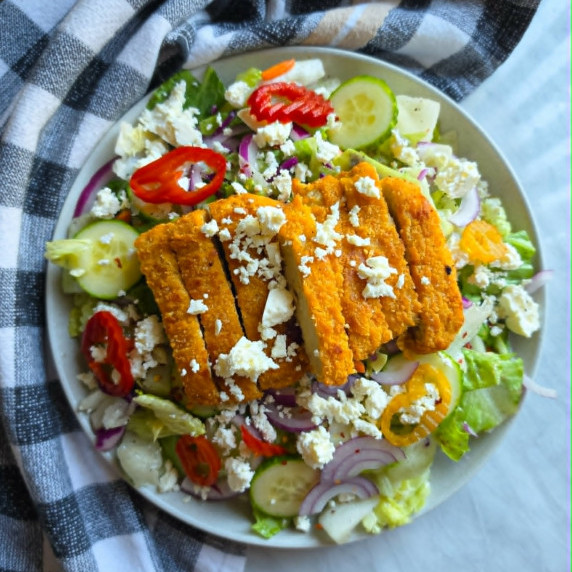 Golden chik'n on a bed of colourful salad against a checkered towel.