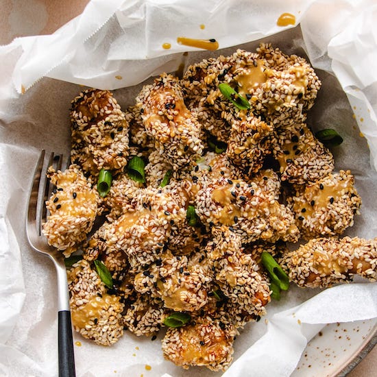 Baked sesame chicken with green onions on paper towel in white plate with fork