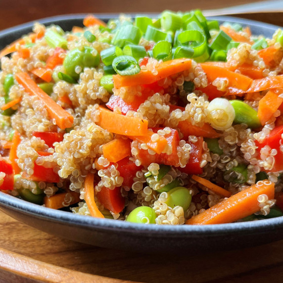 Quinoa salad with carrots, edamame and green onion in a gray bowl.