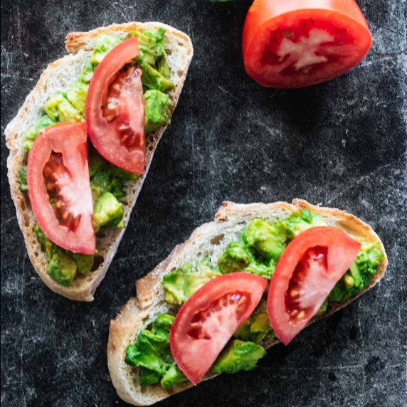 Two slices of avocado tomato toast on a dark marble surface.