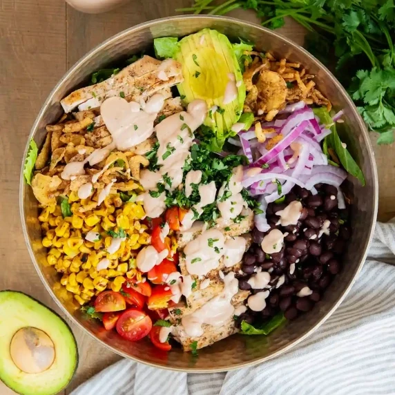 A top shot of a salad bowl with chicken and veggies inside with bbq creamy sauce.