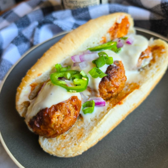 Meatballs dredged in red BBQ sauce and hot white queso on a roll.