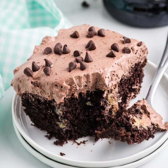 square piece of chocolate baileys poke cake with a piece taken out with fork and resting on plate