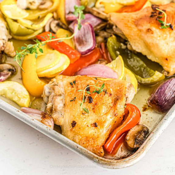 Baked chicken thighs and vegetables close up on the corner of the pan.