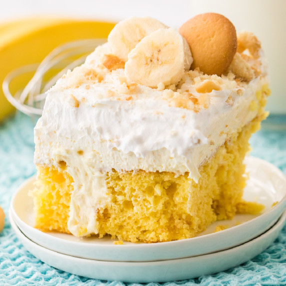 Slice of cake topped with layers of pudding, whipped cream, and vanilla cookies on a plate.