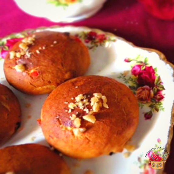 Bath buns topped with sugar on a Royal Albert plate on a red tablecloth with a teapot