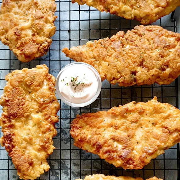 Fried chicken breast recipe pieces laid over a cooling rack over a lined baking sheet.