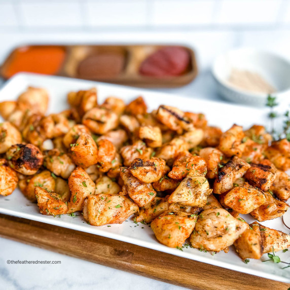 A plate of grilled nuggets with a platter of sauce and a plate of sticks