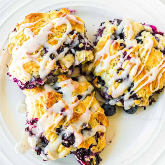 Three blueberry biscuits with glaze on a plate.