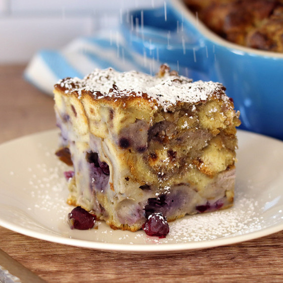 A serving of blueberry cheesecake French toast casserole being dusted with powdered sugar.