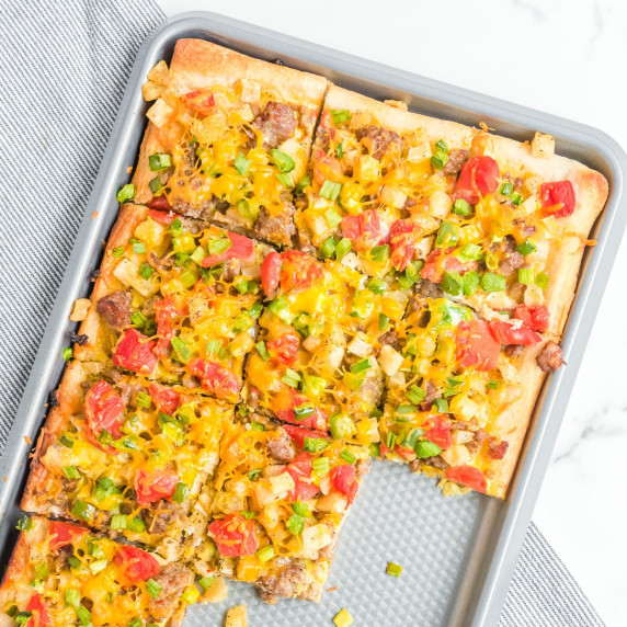 Up close of a rectangular sausage breakfast pizza on a pan missing a few pieces.