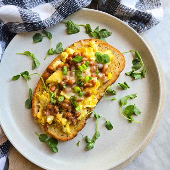 Golden toast topped with yellow eggs, brown beans, and pops of green on a white plate