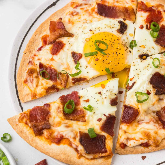 Breakfast tortilla pizza on a plate with green onions as garnish.