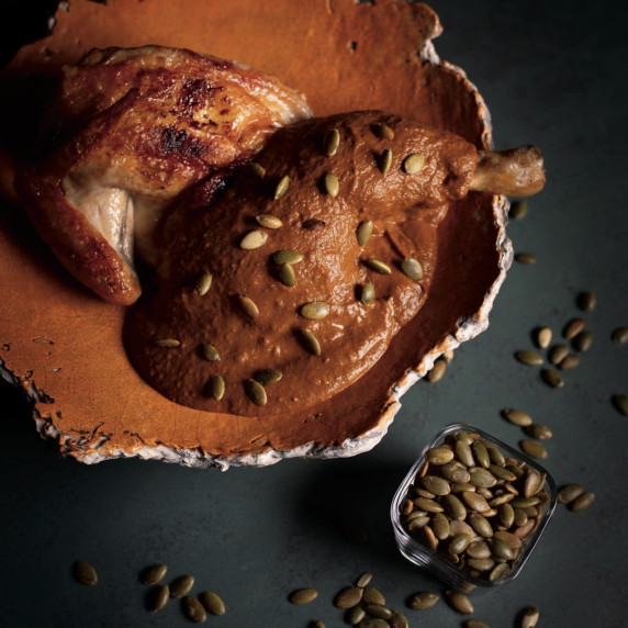 Roasted brined chicken with rich pumpkin mole sauce, garnished with toasted pumpkin seeds.