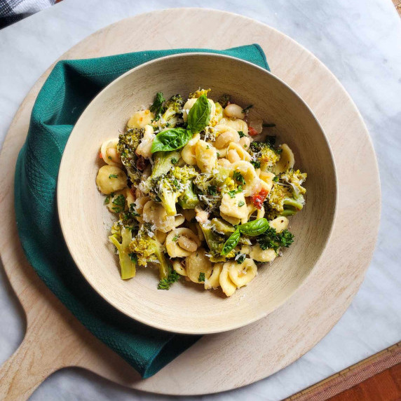 A wooden bowl full of colourful pasta with an emerald green towel against a white marble background.