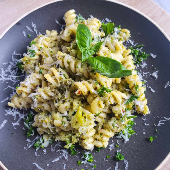 Gorgeous Fusilli tossed in a green broccoli sauce with fresh green herbs on a matte black plate.
