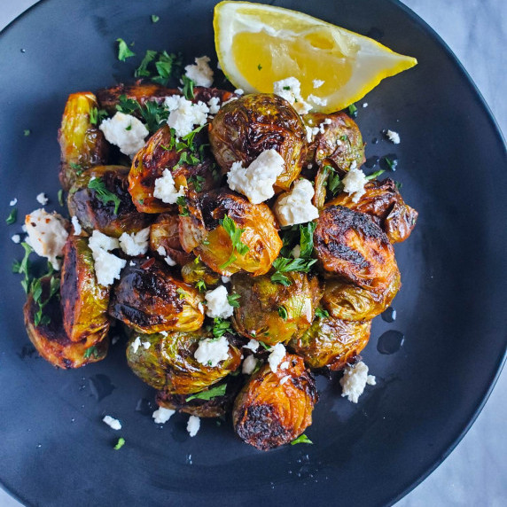 Buffalo sauced brussel sprouts garnished with feta & herbs on a black plate.