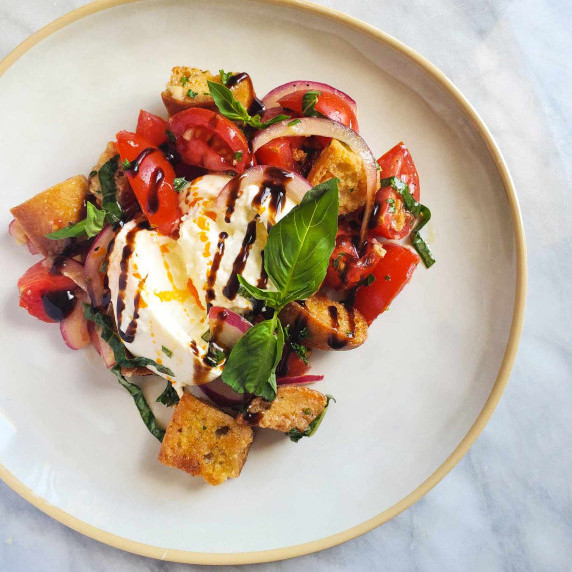 Tomatoes, toasted bread, & white burrata, finished with a dark drizzle of balsamic on a white plate
