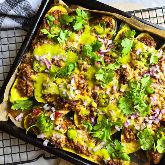 A tray full of gorgeous stuffed zucchini topped with vibrant green salsa and green cilantro.