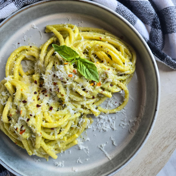 Gorgeous, green bucatini served in a gray rimmed bowl against a checkered towel.