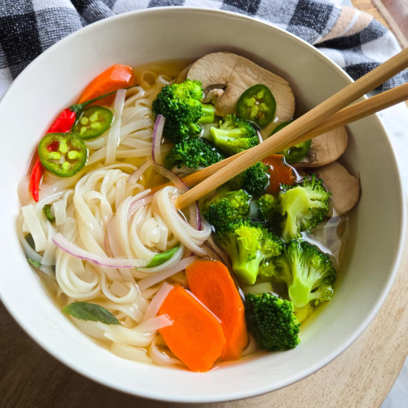 A bowl of noodle soup with colourful veggies against a checkered towel.