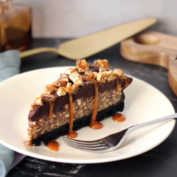 A slice of candy bar pie on a white plate with caramel drizzled over the top
