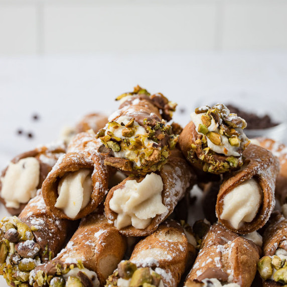 close up of cannoli shells filled with authentic filling and ends dipped in chocolate and pistachios