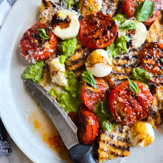 A colourful assortment of veggies, grilled bread, and herbs on a white plate.