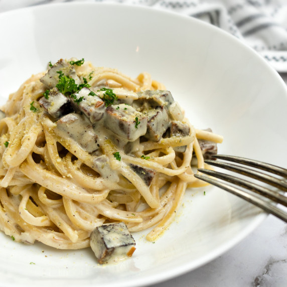 Vegan carbonara pasta topped with creamy sauce and diced vegan bacon, garnished with parsle
