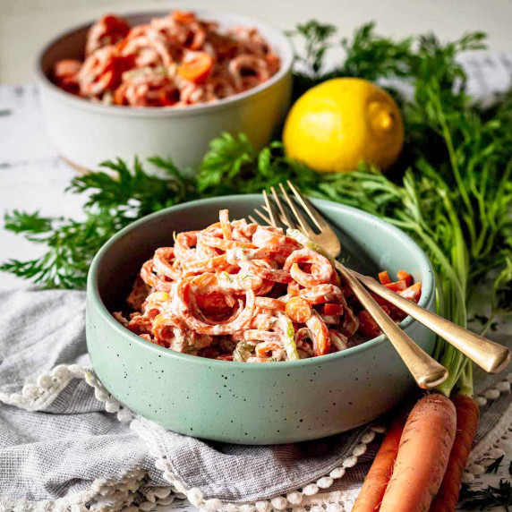 Two bowls of carrot cucumber salad with gold forks.