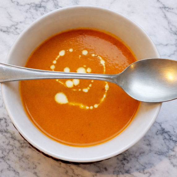 Bowl of roasted carrot and saffron soup with a swirl of cream, photographed on a white surface.