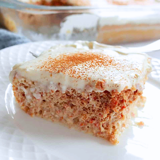 Slice of moist carrot tres leches cake topped with cream cheese frosting and a sprinkle of cinnamon,