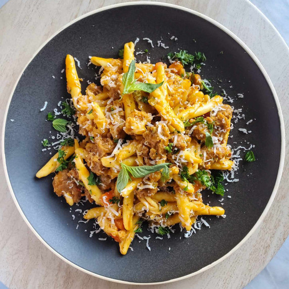 Saucy pasta topped with cheese and green herbs on a matte plate.