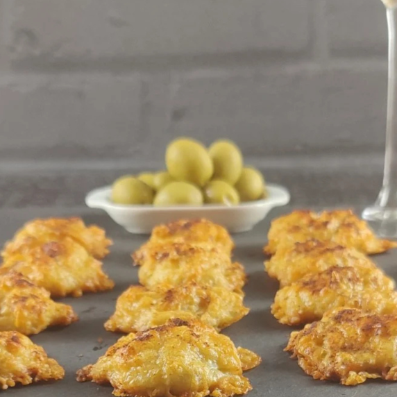 Gruyere Cheese Puffs on a back slate with green olives and a gass in the background