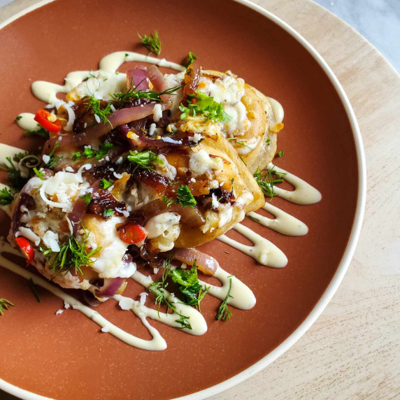Pierogis on a deep orange plate with a white drizzle of ranch and some green herbs.