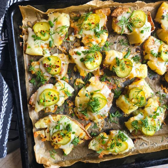 A tray of golden potatoes topped with green herbs and spicy pickles.