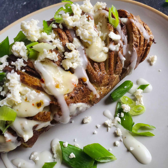 Golden brown potato stuffed with melted cheese on a white plate with green garnishes