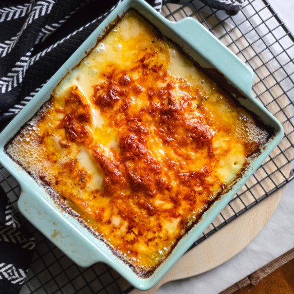 A blue baking dish filled with a golden crusted potato dish with a black towel in the back