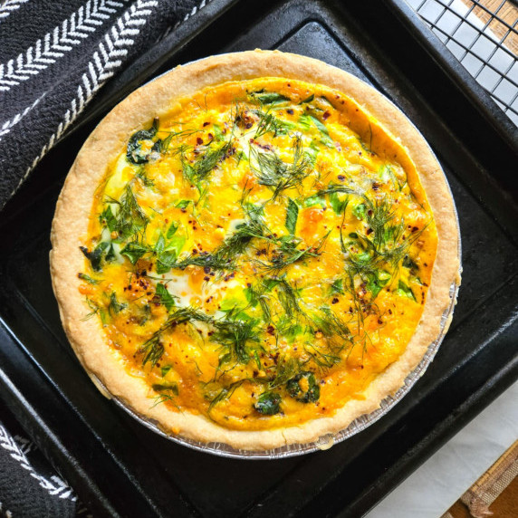 Golden brown quiche with pops of green dill & onions on a black tray.