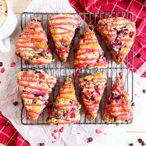 cherry chocolate scones on a wire rack on parchment paper on a red plaid towel with a cup of coffee